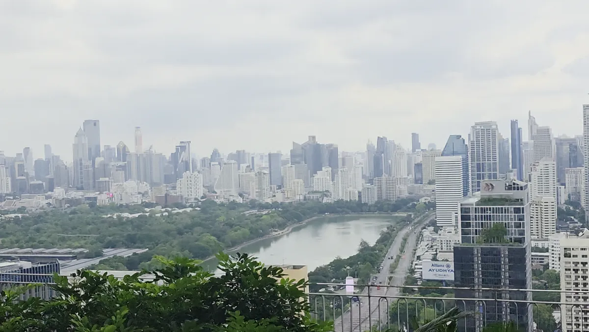 A view from a balcony over a park, a lake, and the Bangkok skyline.