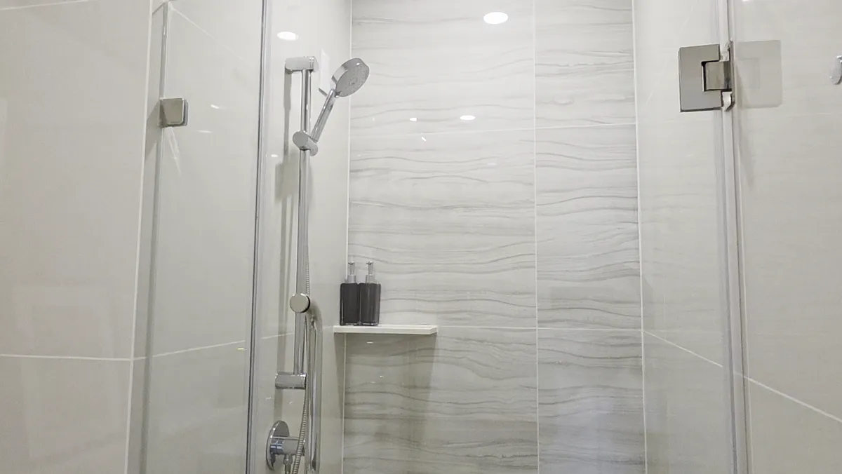 A shower with marble-patterned walls and a handheld shower head.